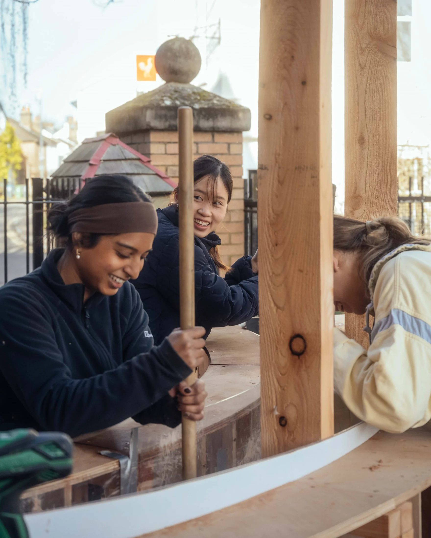 Three students working on the sauna's circular timber form, one holding a long ramming tool