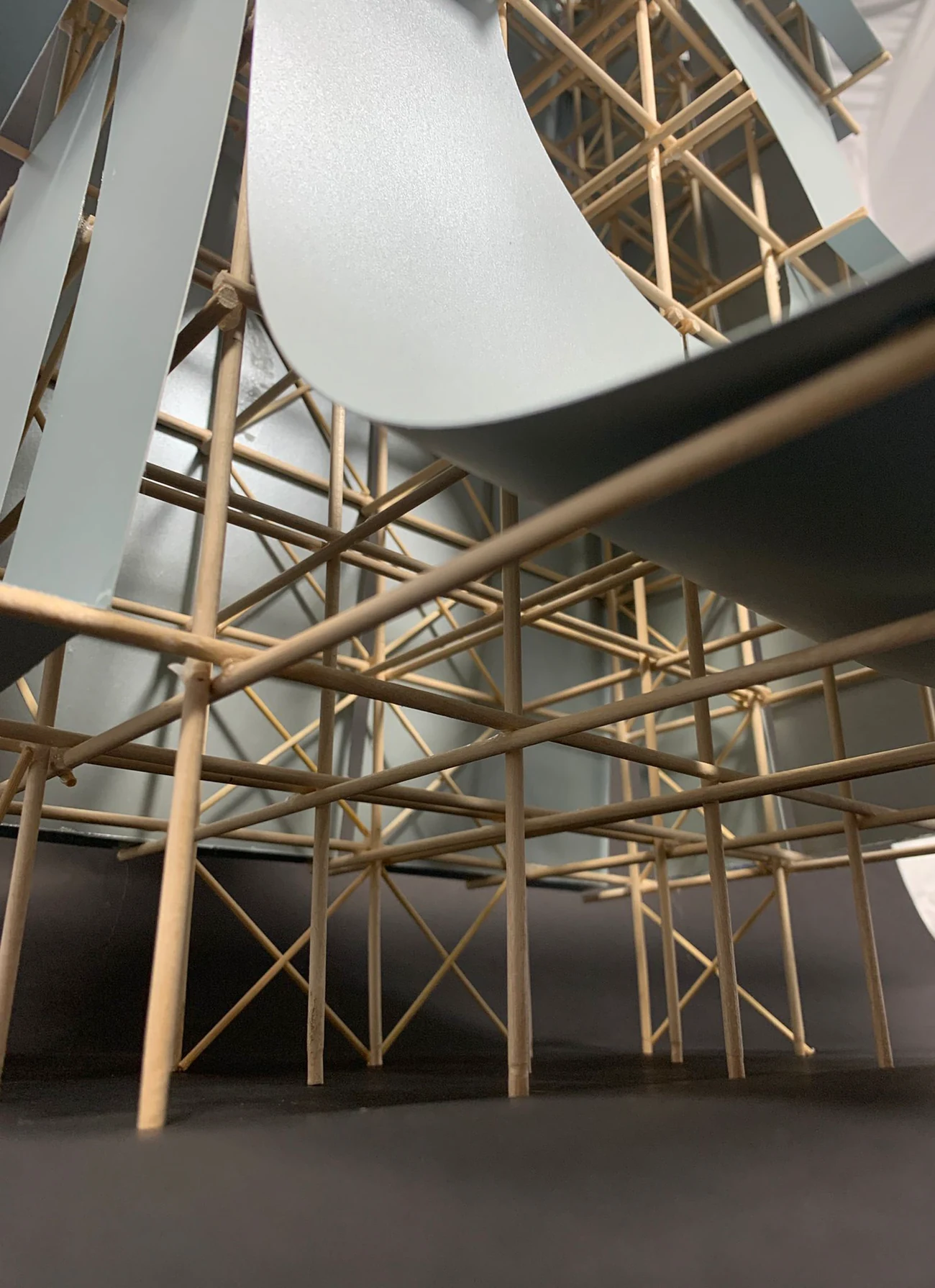 Photograph looking up inside the model, the curved metallic skin sweeping overhead and the bamboo cross-braced frame extending out into the space