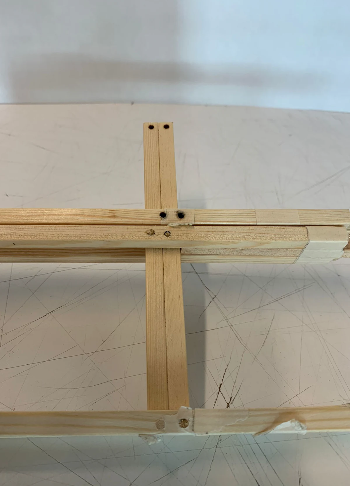 Close-up of a cross-bracing joint, showing two diagonal timbers intersecting a horizontal beam, fixed by small pegs