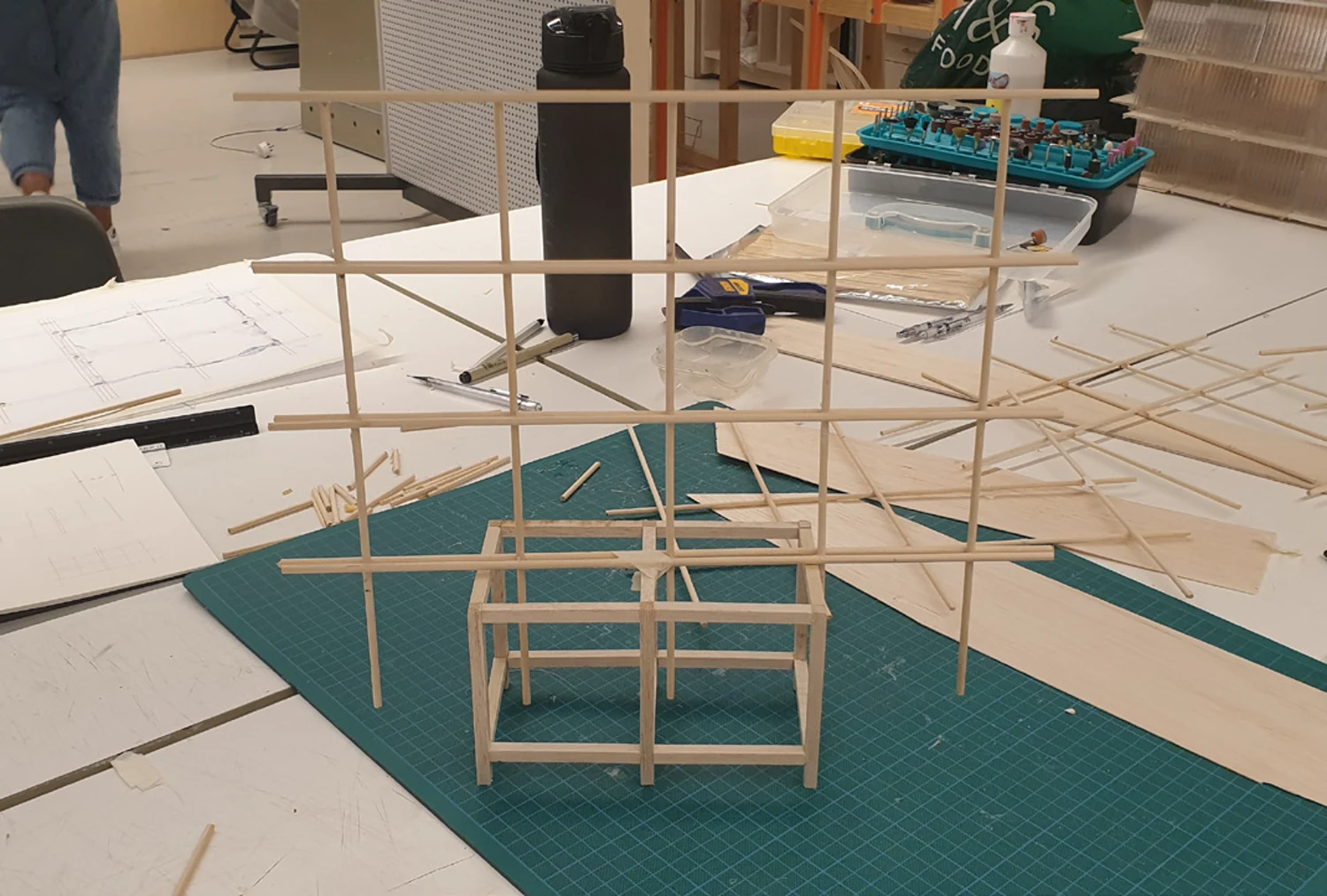 The timber frame under construction on a green cutting mat, showing the cube-gridded structure taking shape