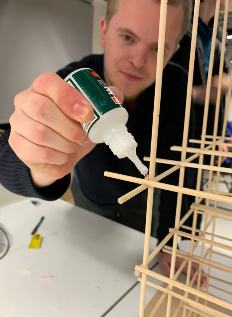 Close-up of hands using a glue bottle to fix a timber joint in the model