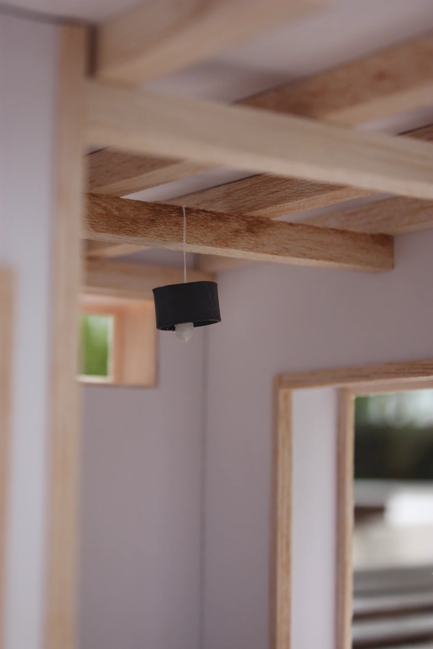Detail of the model interior — exposed timber roof beams above, a small pendant light, planting visible through the side opening