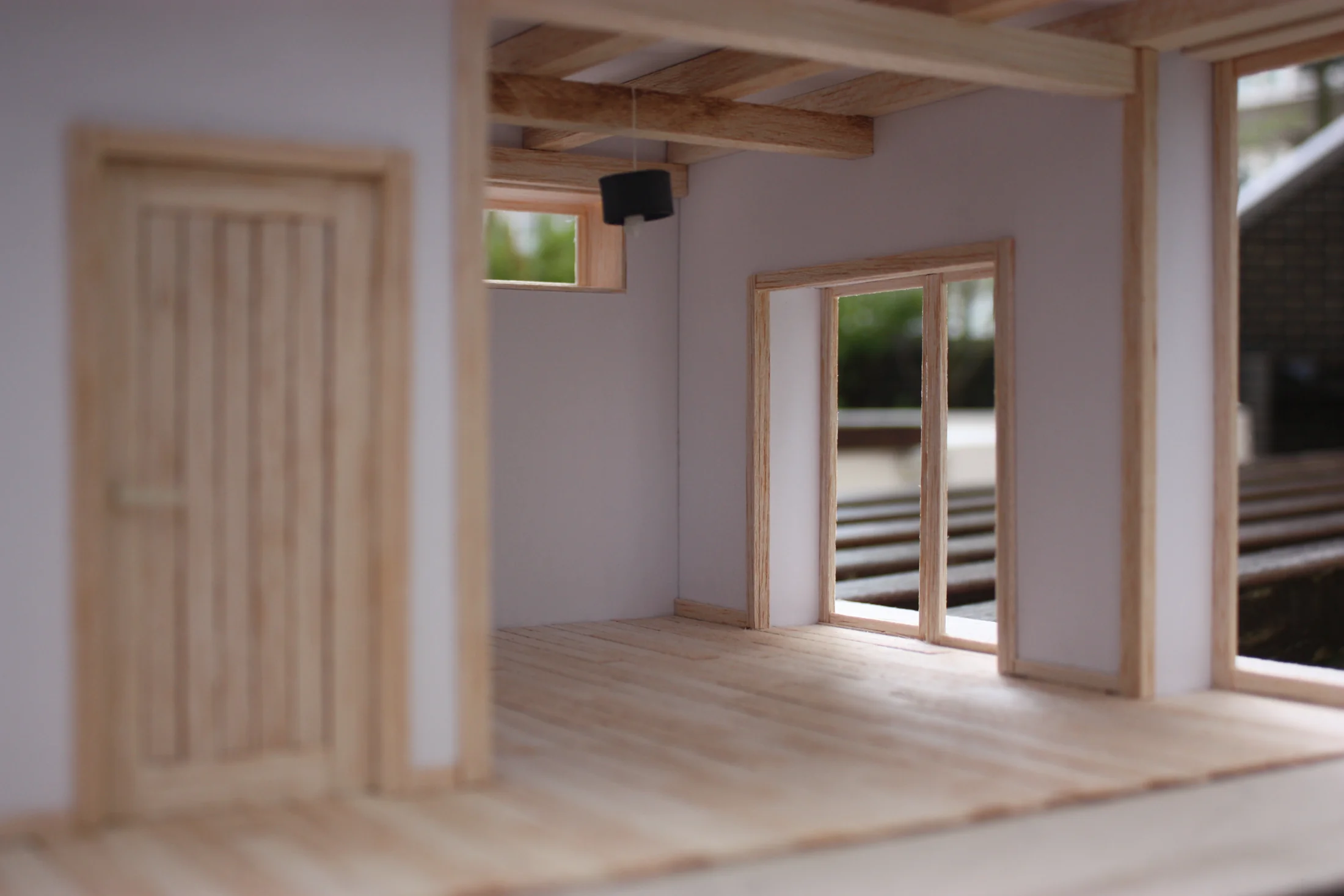 Physical model of the same dwelling interior — timber-framed walls and roof, doors to the planted terrace