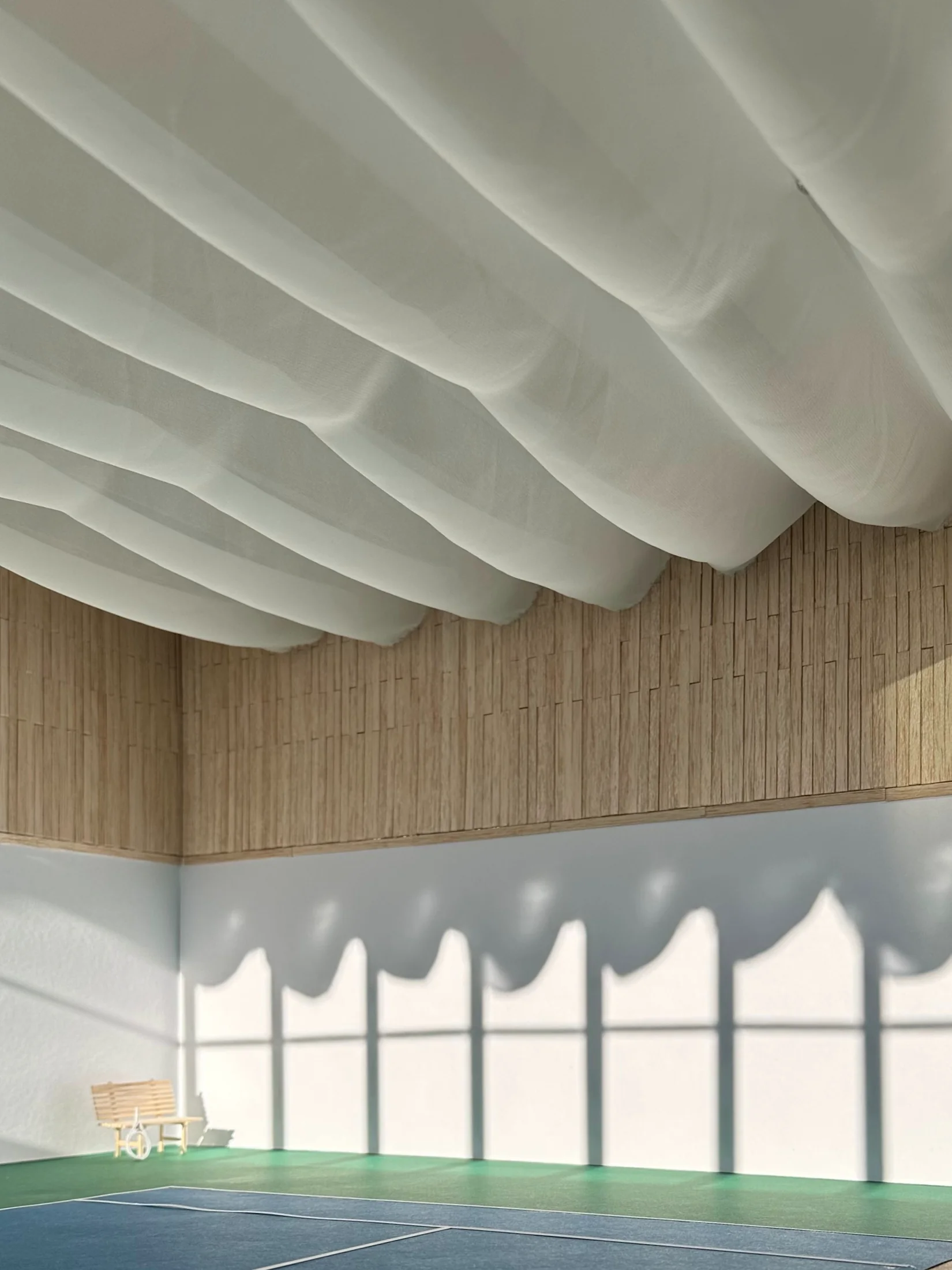 Interior of the sports hall with a wavy white ceiling and louvre shadows cast across the lower wall above the green and blue court